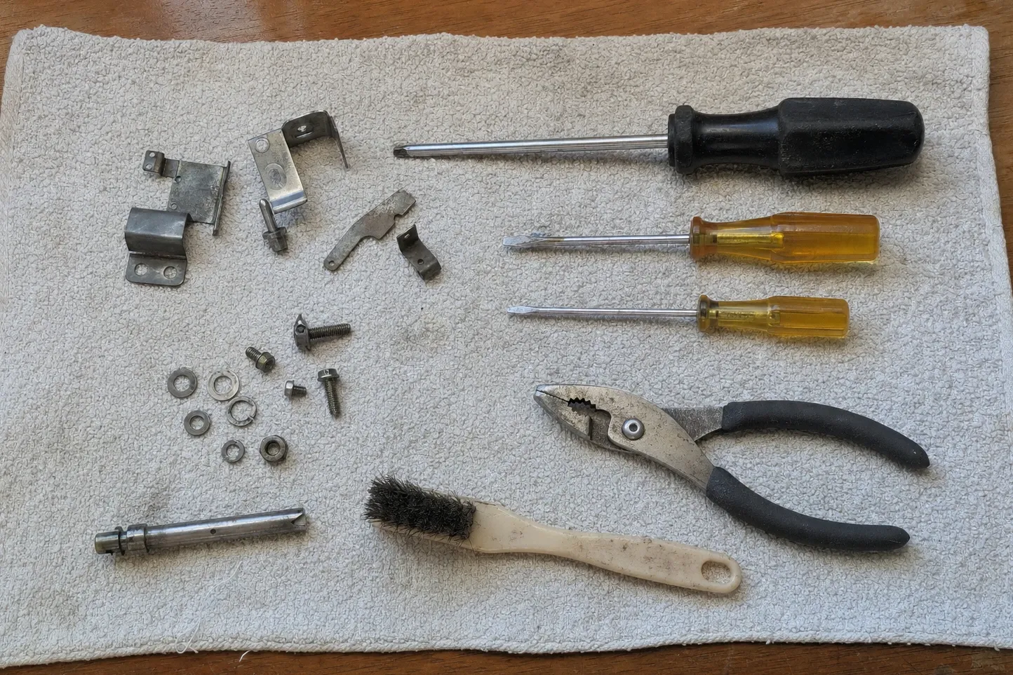 Latch and hinge brackets, an orifice holder, screws and washers set out beside screwdrivers, pliers and a wire brush