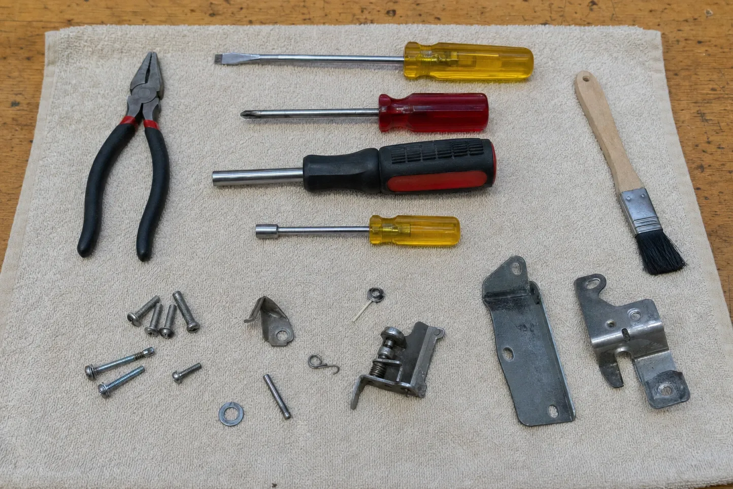 Spring-loaded door latch, a long slotted hinge strap and a stamped hinge bracket set out on a towel with roll pins, springs and screws